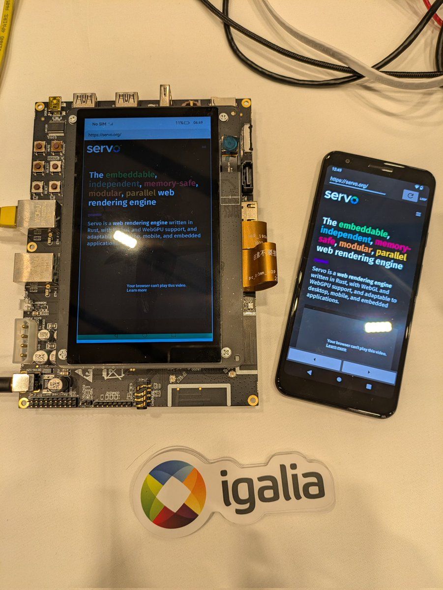 Picture of a Rockchip board and an Android phone, both running Servo and showing the servo.org homepage. At the bottom of the image there are some stickers with Igalia logo.