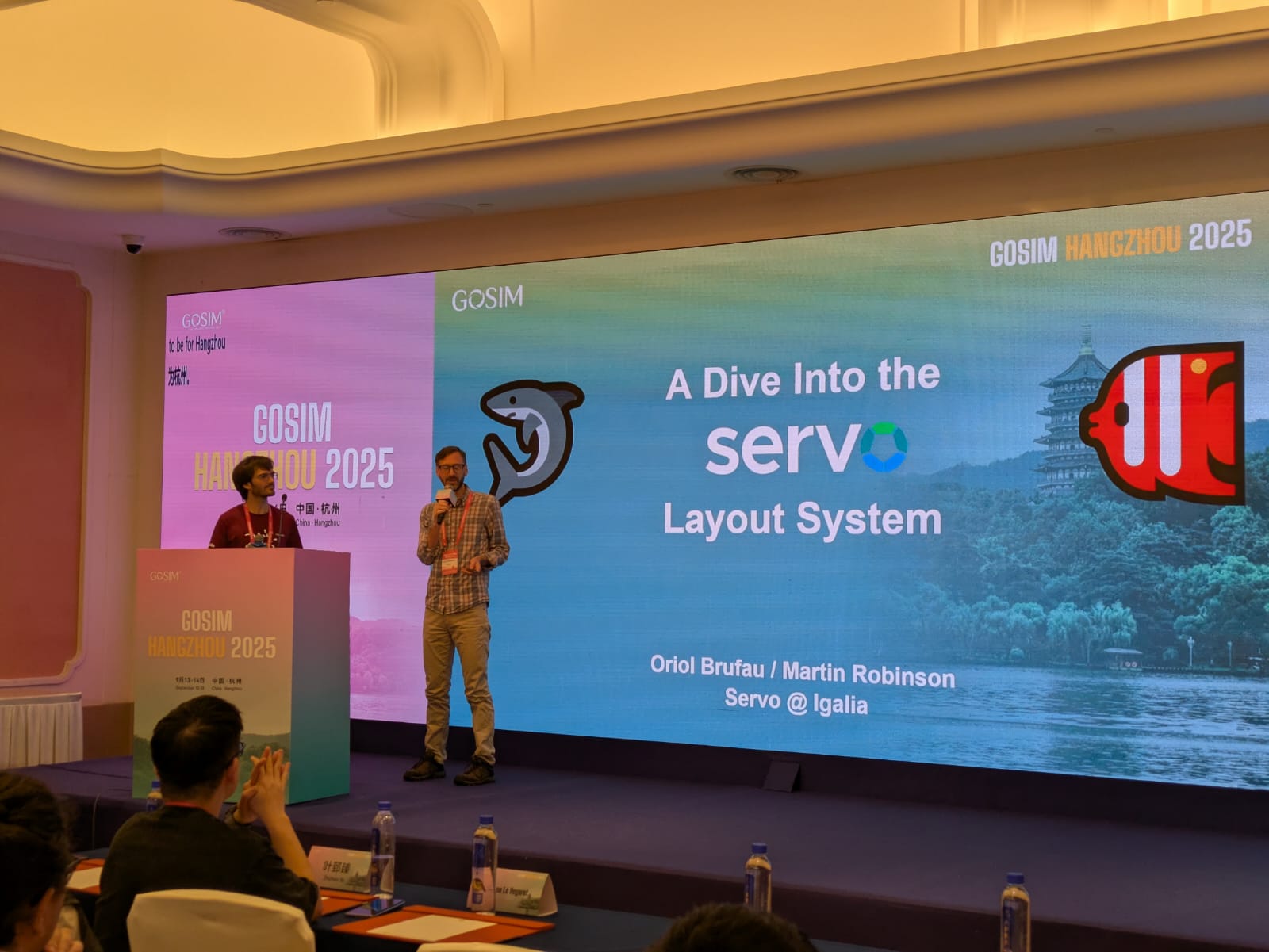 Picture of Oriol Brufau and Martin Robison on stage, with the fist slide of their talk call "A dive into the Servo layout system"